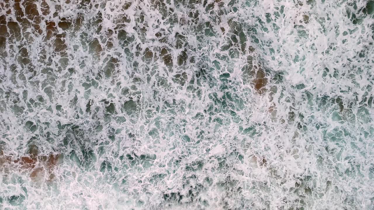 Aerial view of a wave breaking on a golden sandy beach, The mesmerizing patterns of foam and surf