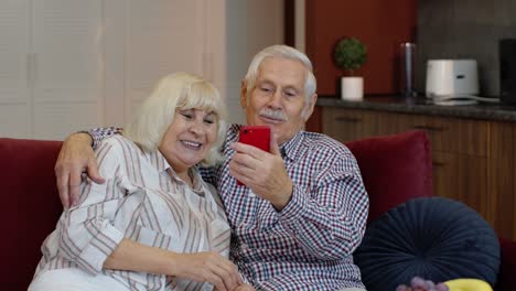 Grandmother-and-grandfather-making-video-call-online-on-mobile-phone-at-home.-Smiling-senior-couple