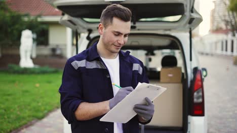 Delivery-service-worker-makes-notes-on-documents-and-standing-on-the-street-near-the-minivan