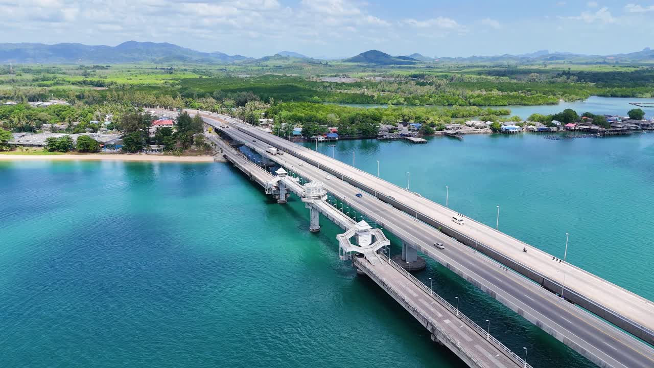 Drone footage captures Sarasin Bridge in Phuket, Thailand, showcasing turquoise waters and lush landscapes under bright daylight