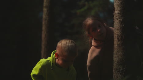 children hide behind tree in night wood. scared little boy and girl lost in wild park in evening. preschooler kids threatened by loneliness and darkness