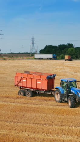 big empty tractor moves by the mowed field. vast farmlands of harvested wheat with hay bales at backdrop. vertical video