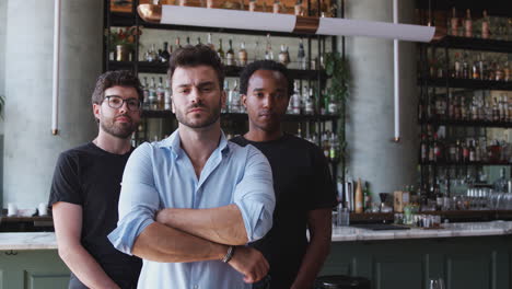 Portrait-Of-Male-Owner-Of-Restaurant-Bar-With-Team-Of-Male-Waiting-Staff-Standing-By-Counter