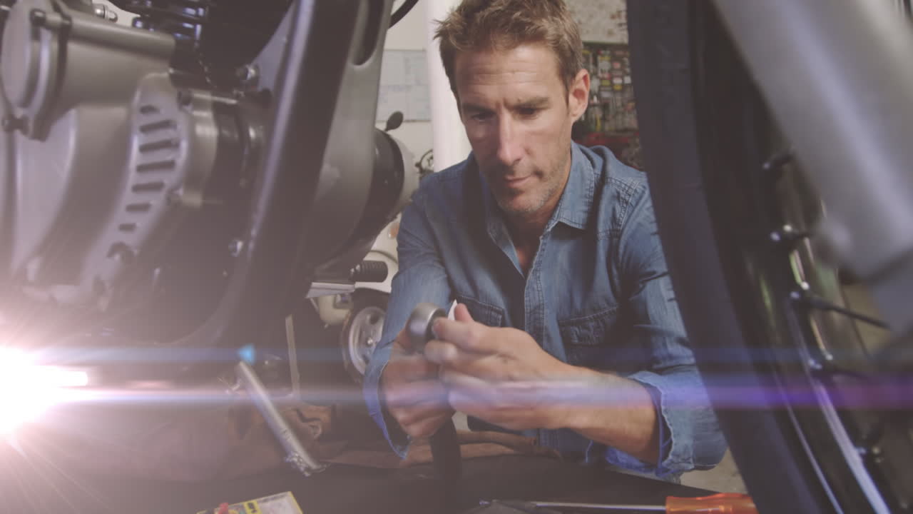 animación de luces brillantes sobre un mecánico caucásico reparando una motocicleta en un garaje