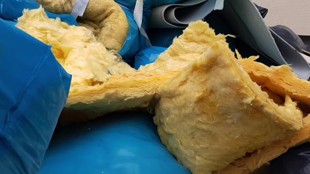 건설 현장에서 파란색 플라스틱 쓰레기 봉투에 있는 유리 섬유 단열재 쓰레기를 가까이에서 볼 수 있습니다.