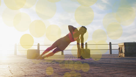 Animation-of-yellow-spots-over-biracial-woman-exercising-on-promenade