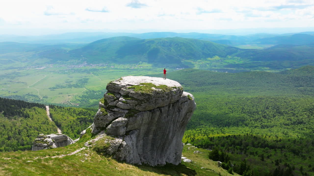 Person standing on a clifftop overlooking a vast mountain landscape