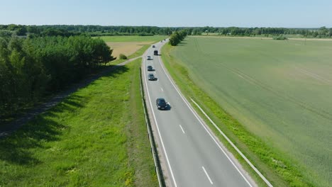 aerial establishing shot of a rural landscape, countryside road with trucks and cars moving, lush green agricultural crop fields, sunny summer day, wide drone shot moving backward