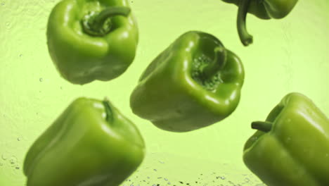 slow motion of green peppers falling into water surface on green background