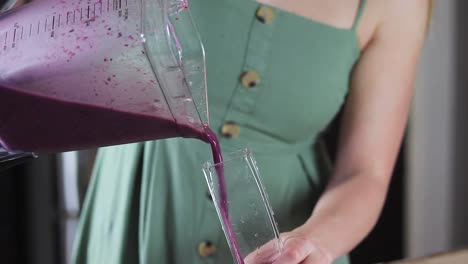 slow motion tight shot of a young women pouring a purple blueberry smoothie into a glass cup in her kitchen