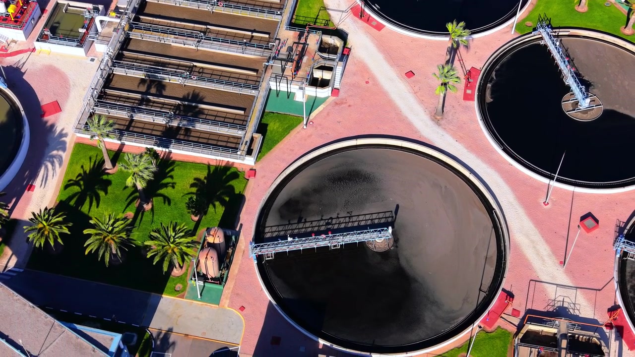 Technical aerial shot of sewage treatment architecture featuring rectangular biological basins and circular secondary clarifiers. Rectangular filtration basins and circular clarifier tank overhead.