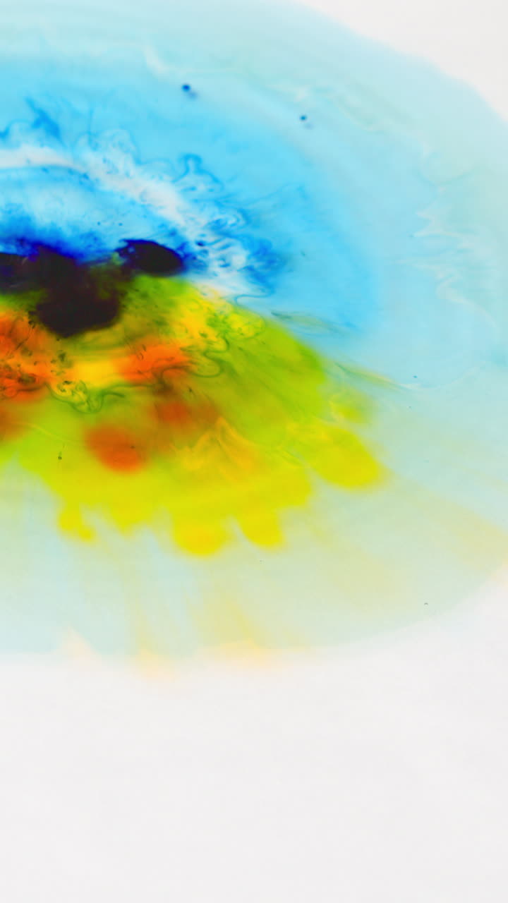 tomada de video vertical aérea de gotas de pintura o tinte amarillo y azul caídas en el agua contra un fondo blanco para crear un patrón de colores giratorios
