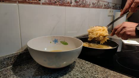 the cook's hands with kitchen utensils remove potatoes cooked in olive oil and mix them with the beaten egg in the bowl, cook spanish omelette in ceramic hob, shot blocked close-up, galicia, spain
