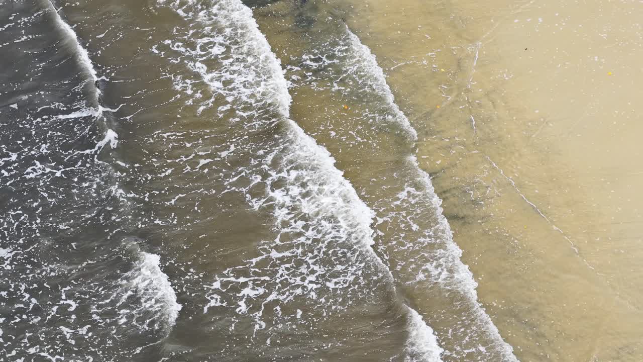 Aerial view of turbulent sea meeting sandy coastline