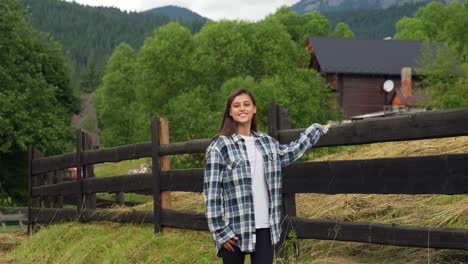 mujer de pie junto a una valla de madera en un campo montañoso