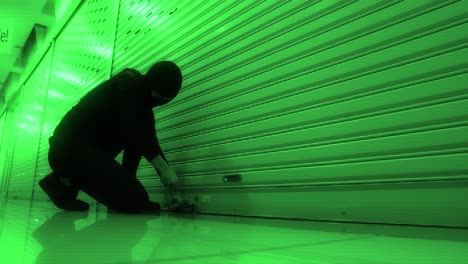 cat burglar breaking in to a store or storage locker by picking the lock while wearing a hood and balaclava - security camera view