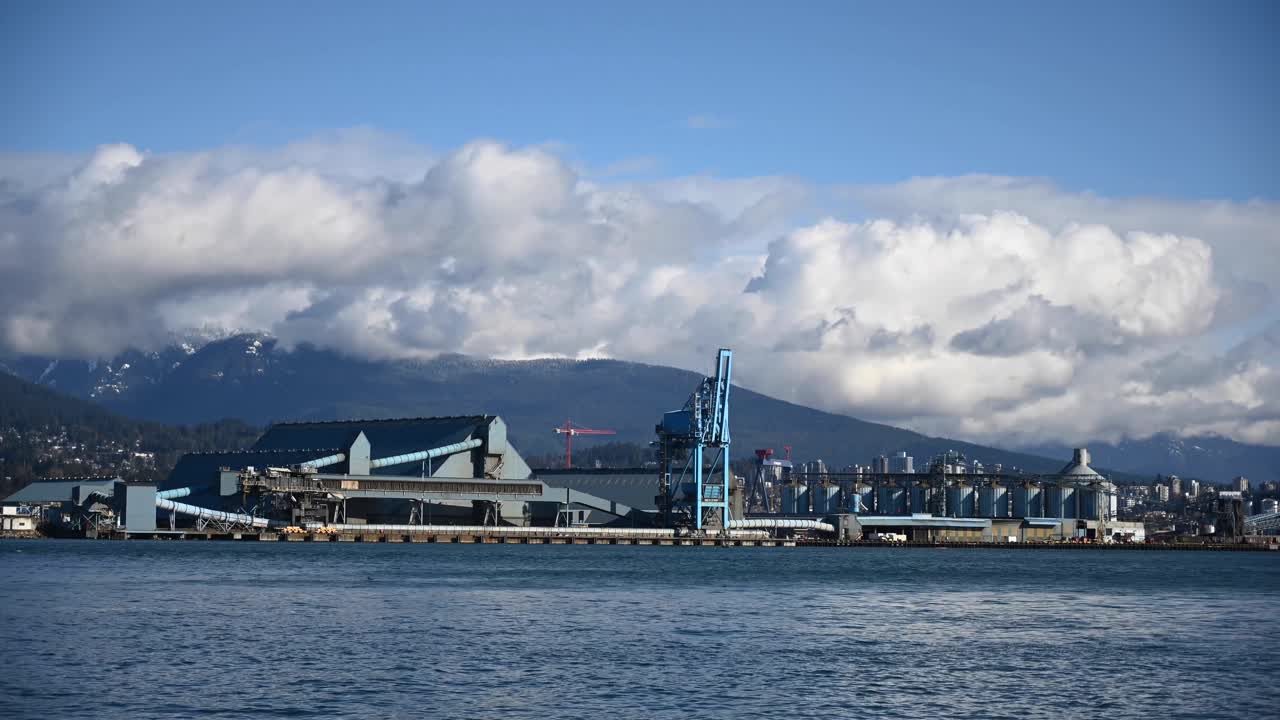부분적으로 흐린 날 배경에 곡식 터미널과 구름이 산 위로 굴러다니며 밴쿠버 항구를 항해하는 작은 흰색 범선