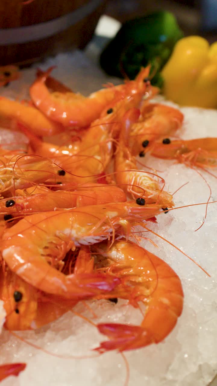 Metal tongs pick up fresh cooked prawns from a bed of ice at a buffet