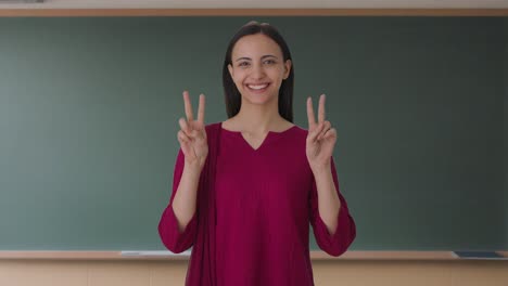 una feliz maestra india mostrando el signo de la victoria