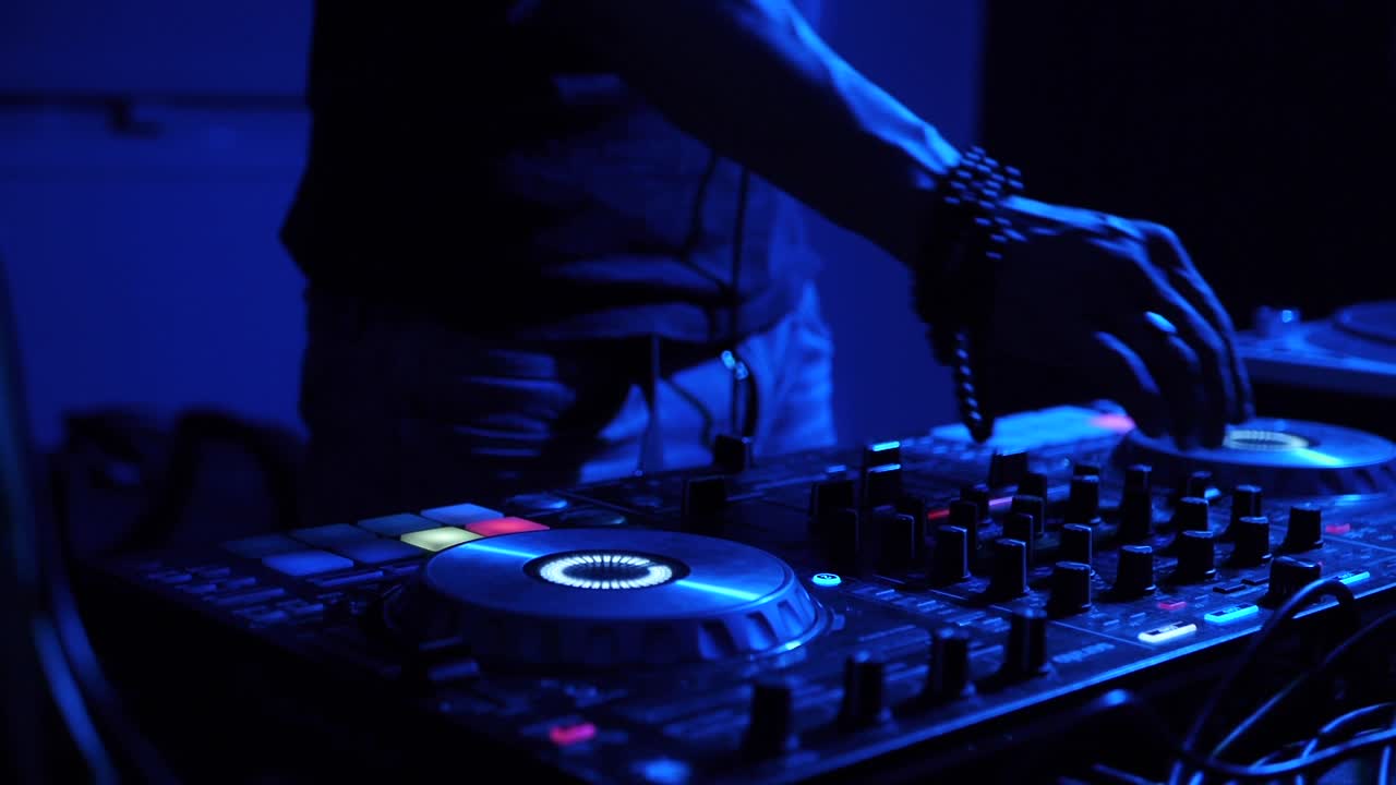 manos y dedos del hombre sincronizando y ecualizando la configuración en la consola de mezclas de dj digital filmada en interiores con iluminación azul dura como primer plano