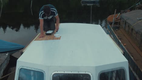 young man painting wheelhouse cabin of wooden boat with primer