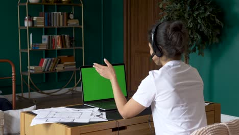 a young indian woman uses a laptop with a green screen works online conference call, training with people, bright room at home