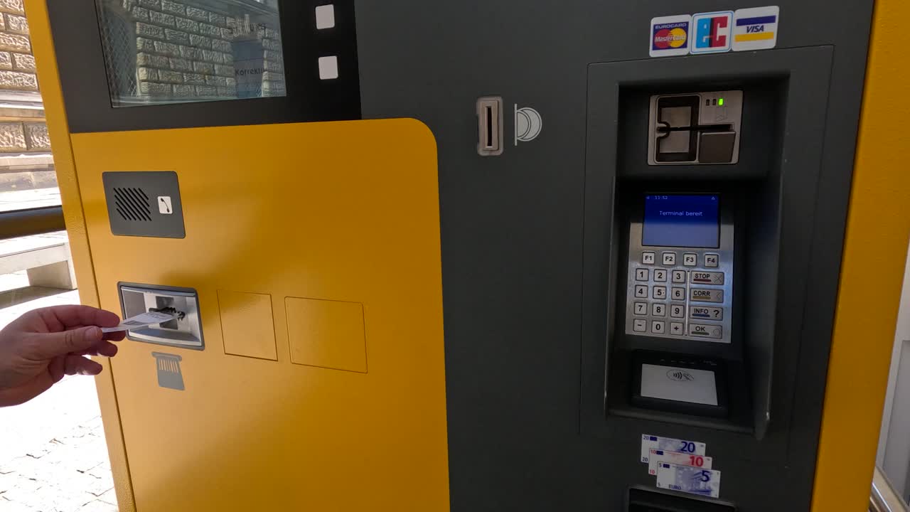 Person inserts card into yellow outdoor ticket machine payment terminal in daylight, close-up
