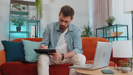 joven empresario que trabaja con computadora portátil y documentos, planeando el presupuesto de gastos en casa
