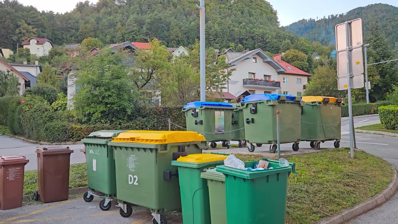 Colorful recycling bins and waste containers placed on street corner in residential area with houses and greenery