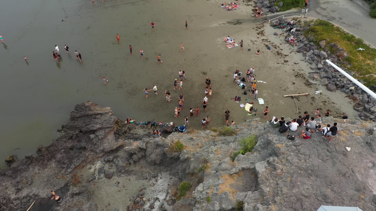 Coastal aerial shot tilting down to reveal people latin dancing on the beach.