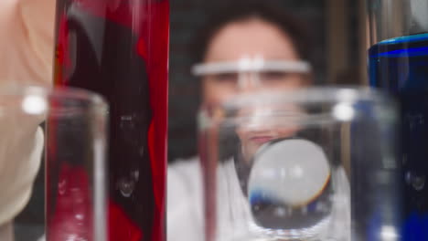 worker with magnifying glass checks red liquid in test tube