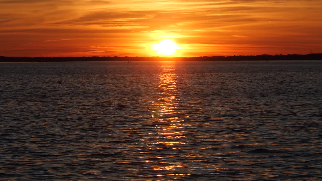 Glowing sun in orange sky setting beyond calm rippling sea horizon