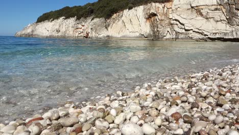 low angle on rocky beach floor and clear water waving, cliffs as backdrop