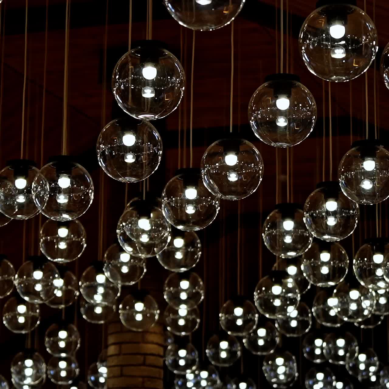 Many light bulbs lighting up. Dark background with lamps becomes bright. Beautiful ceiling with round glass lamps switches on.