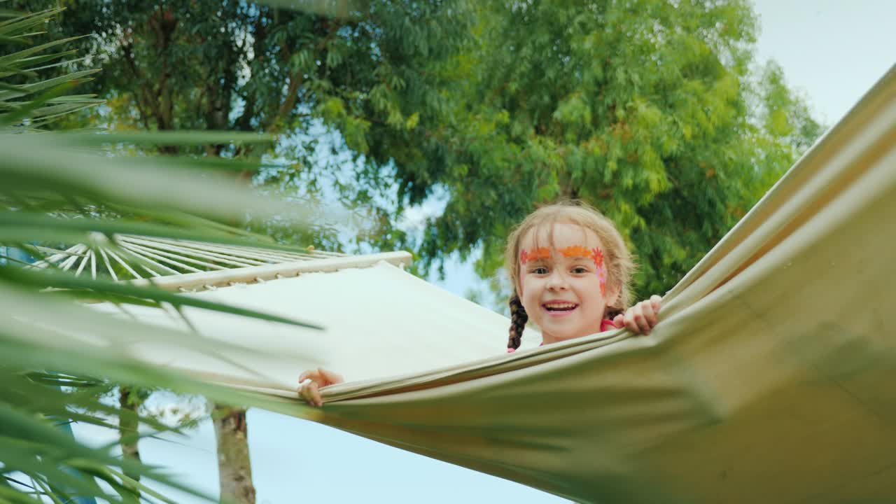 niños divertidos con caras pintadas montan en una hamaca en el territorio del hotel en la playa