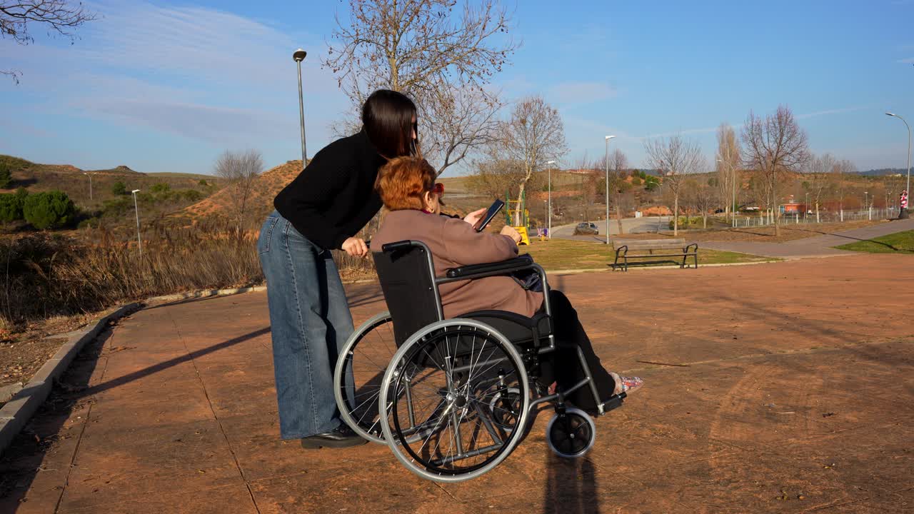 Granddaughter takes a selfie with her granny in wheelchair on a sunny day