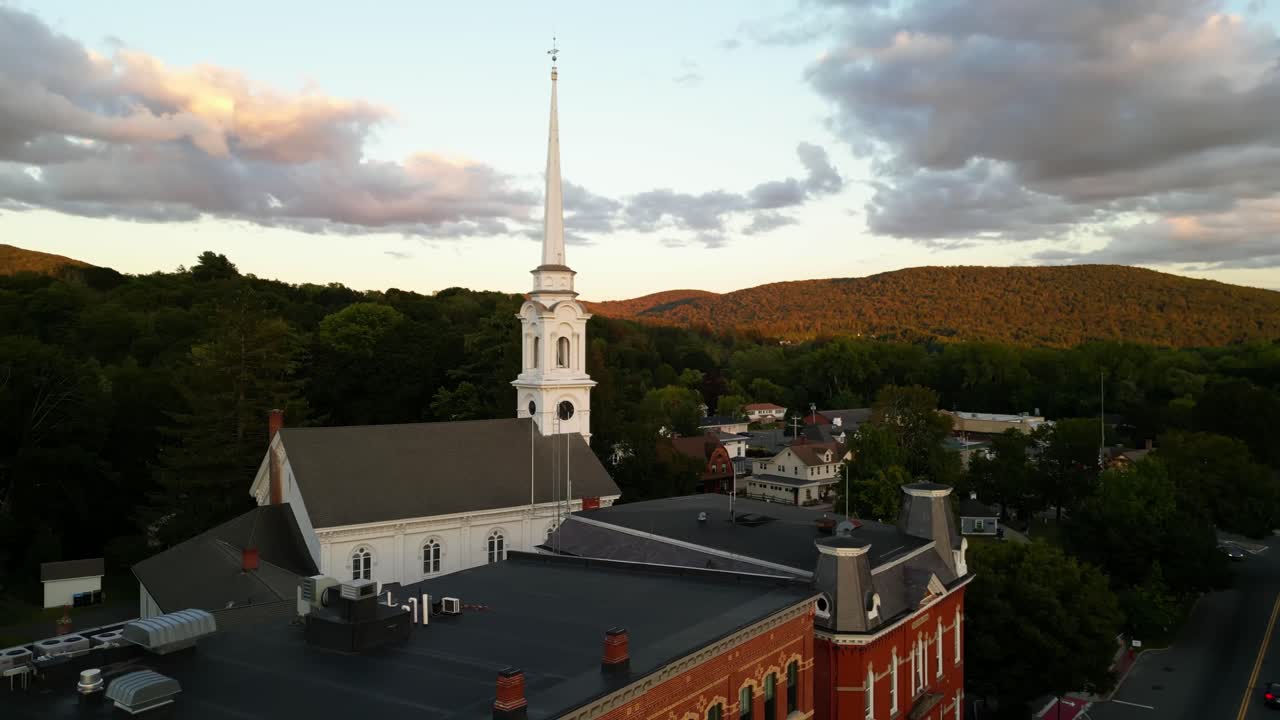 Aerial rising shot of White First Congregational Church in American town with golden green mountains at sunset time. Lee Town, Massachusetts, United States in Autumn Season. Panorama wide shot