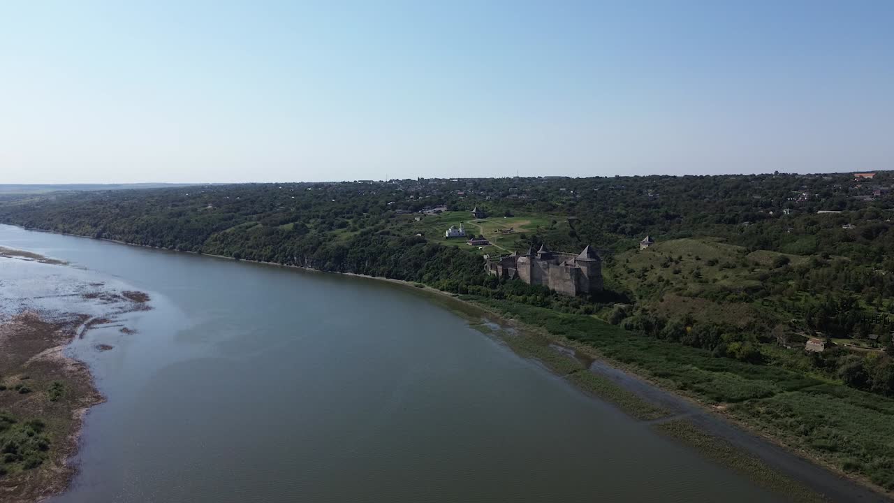 Riprese cinematografiche con drone che catturano la Fortezza di Khotyn da oltre il fiume, rivelando l'intera portata della roccaforte medievale sullo sfondo del paesaggio naturale.