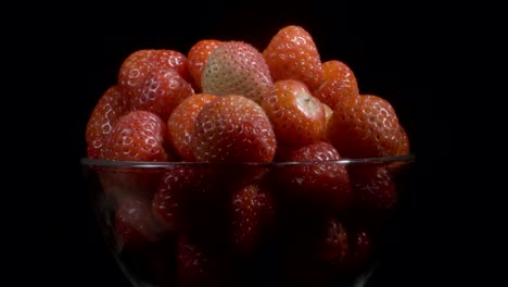 rotate of red strawberries in glassware on black background. camera rotation 360 degrees, close-up.