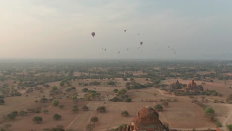 Morning-scenery-at-Dhammayan-Gyi-Temple-with-distant-hot-air-balloons,-aerial