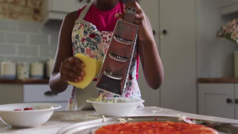 african american girl making pizza grating cheese in kitchen