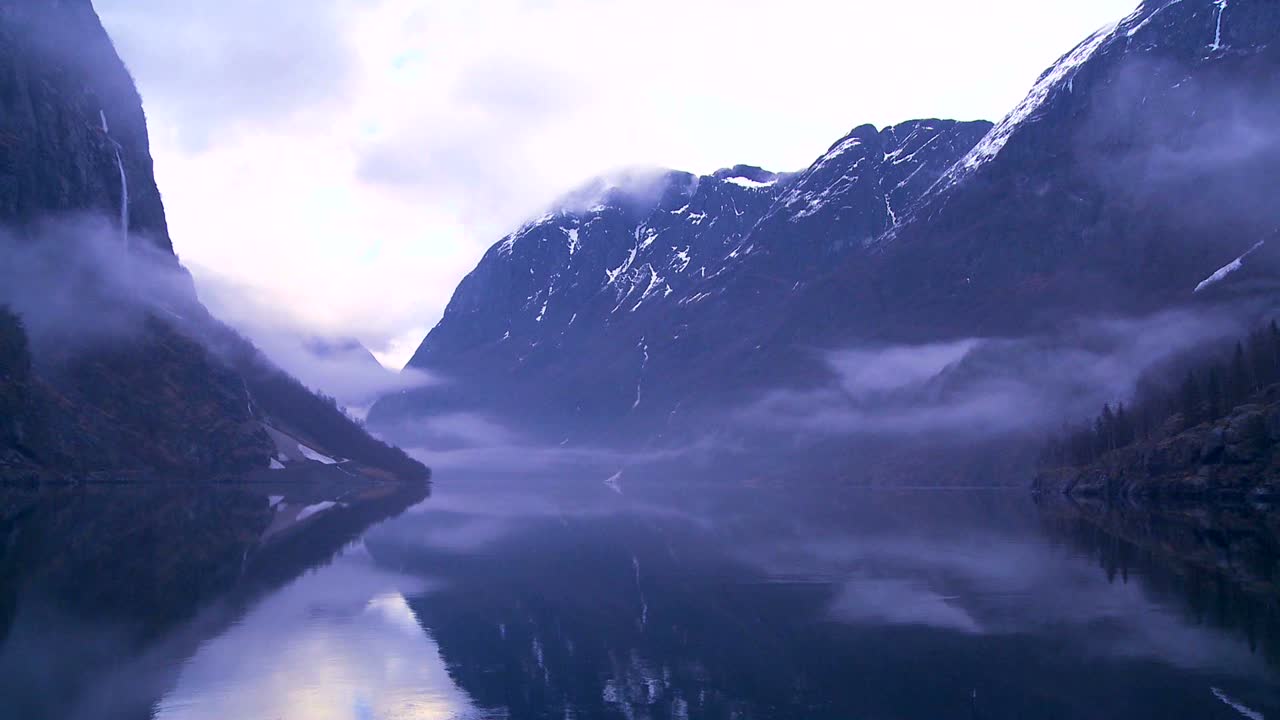 tåge og skyer hænger i norges fjorde.