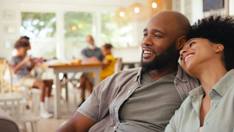 Couple-At-Home-On-Sofa-Streaming-Show-Or-Movie-To-TV-With-Multi-Generation-Family-In-Background