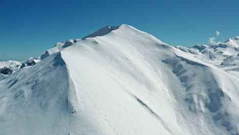 Bright-snowy-mountain-peak-under-a-clear-blue-sky,-crisp-and-serene-in-broad-daylight,-aerial-view