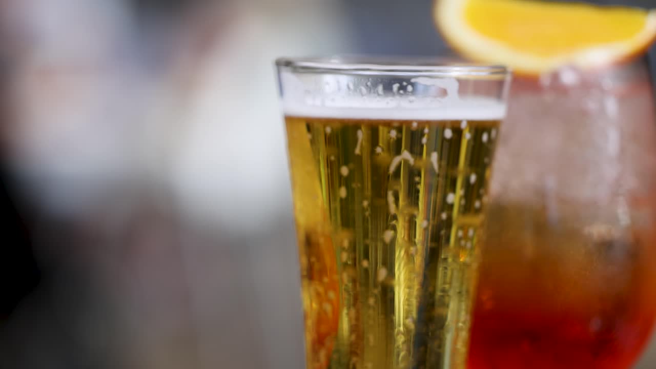 Close-up of a beer and Aperol spritz with lemon and lime garnish, highlighting bubbles and condensation in a vibrant setting