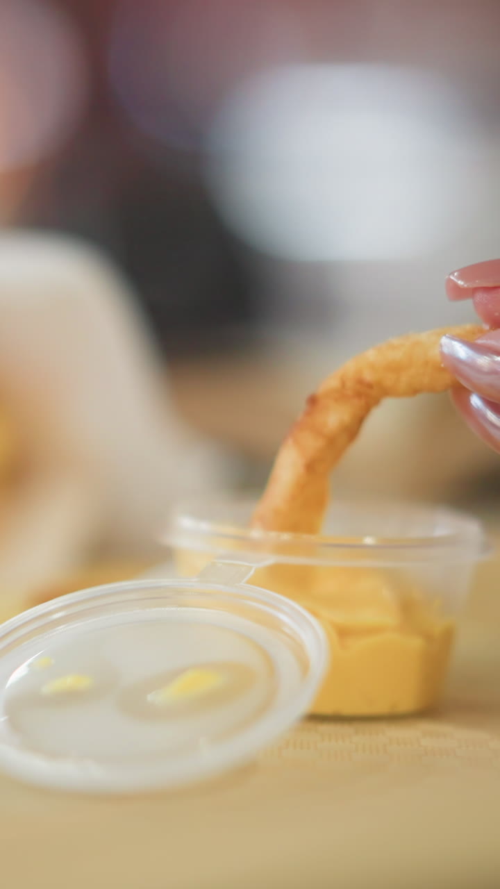 primer plano de la mano sumergiendo patatas fritas crujientes en una salsa de queso cremosa en un recipiente para llevar, con el fondo borroso creando una atmósfera cálida e indulgente en un entorno casual