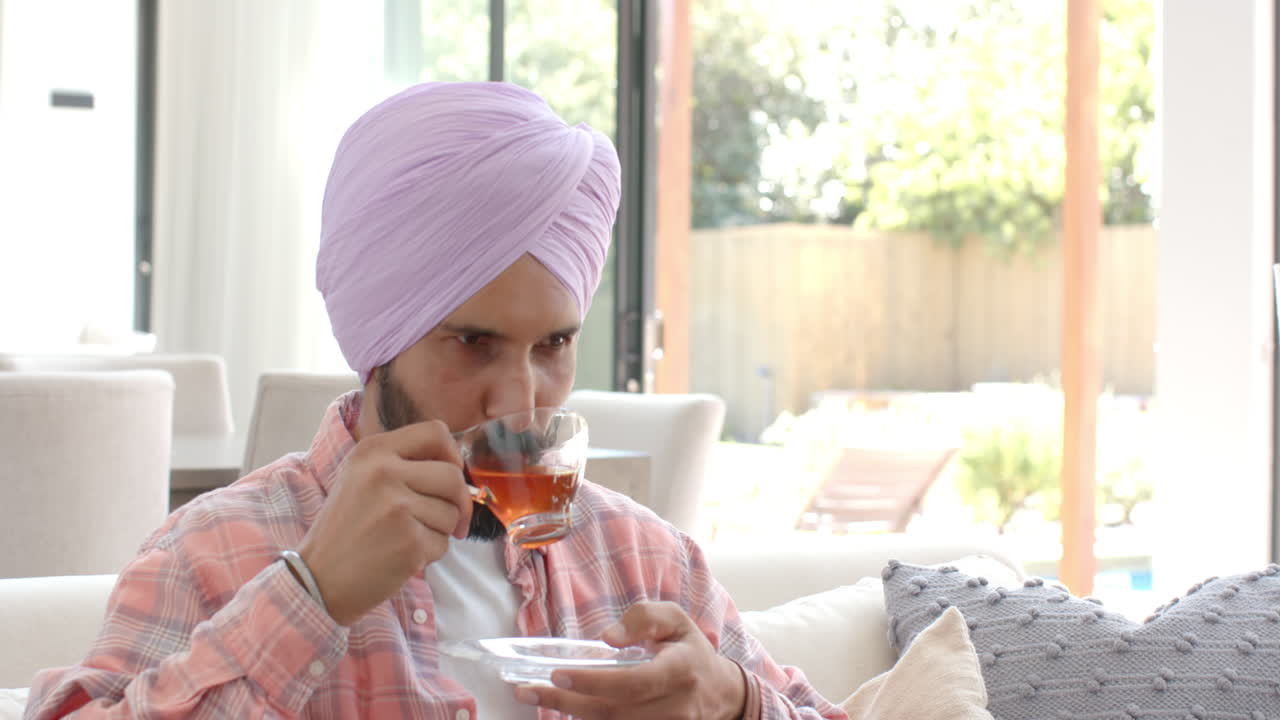 Drinking tea, Indian man in turban relaxing on sofa at home