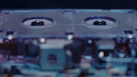 carretes de grabadora de microcassette en movimiento con componentes internos expuestos visibles en primer plano bajo una luz azul fría