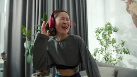 asian woman playing air guitar and wearing headphones to listen to music, having fun at home