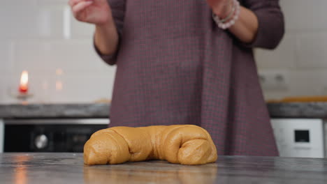 lower body view of woman finishing kneading dough as she removes hands, leaving shaped dough on kitchen counter with blurred background featuring warm lighting and modern kitchen appliances